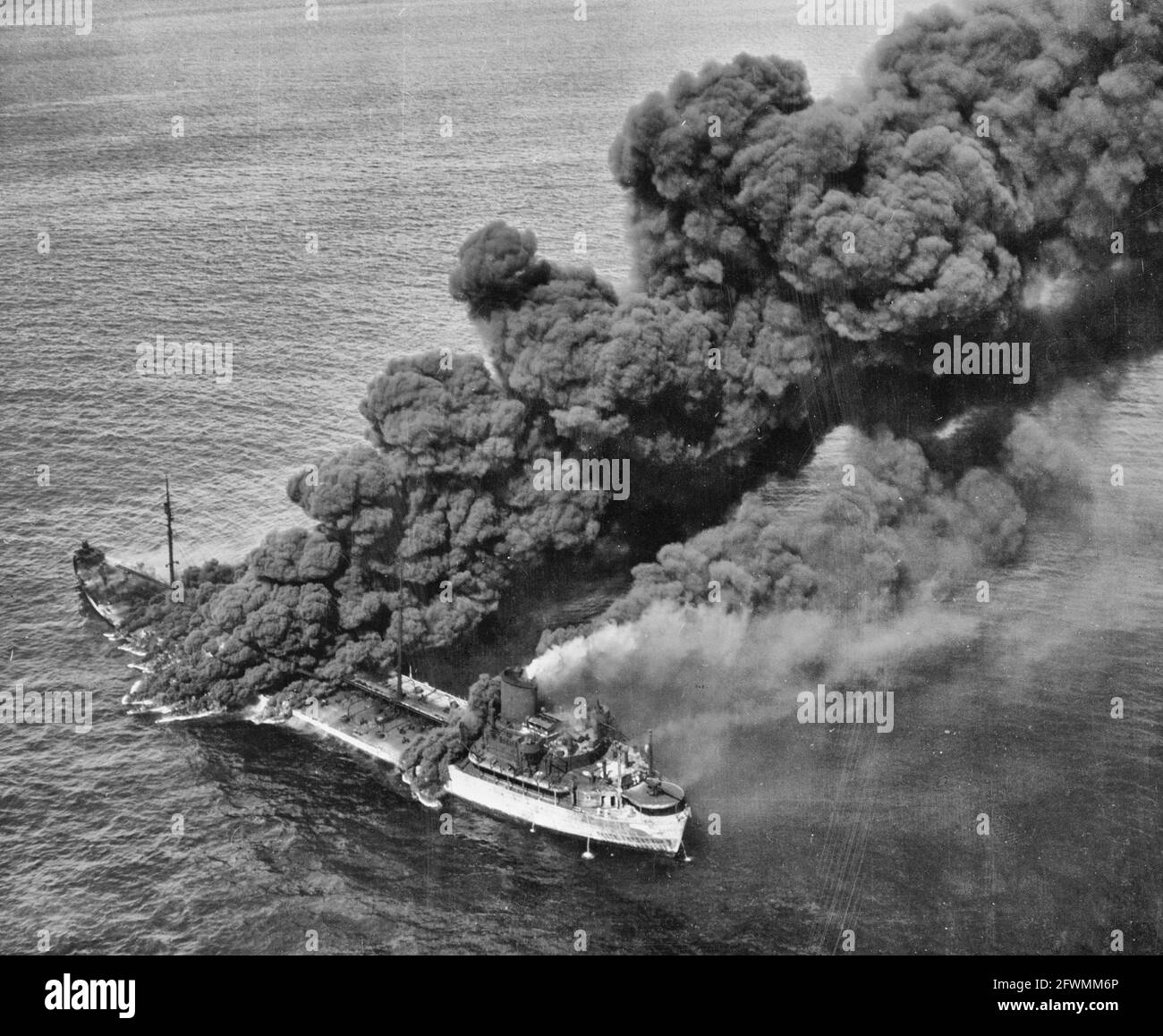 A United States tanker torpedoed by an Axis submarine. Despite a raging fire which sent columns of black, oily smoke billowing into the sky, crew members were able to bring the flames under control and the tanker was towed to port by a United States Naval ship. The tanker is now in an east coast ship yard being repaired and soon will be back in active service aiding the nation against its enemies - World War II Stock Photo