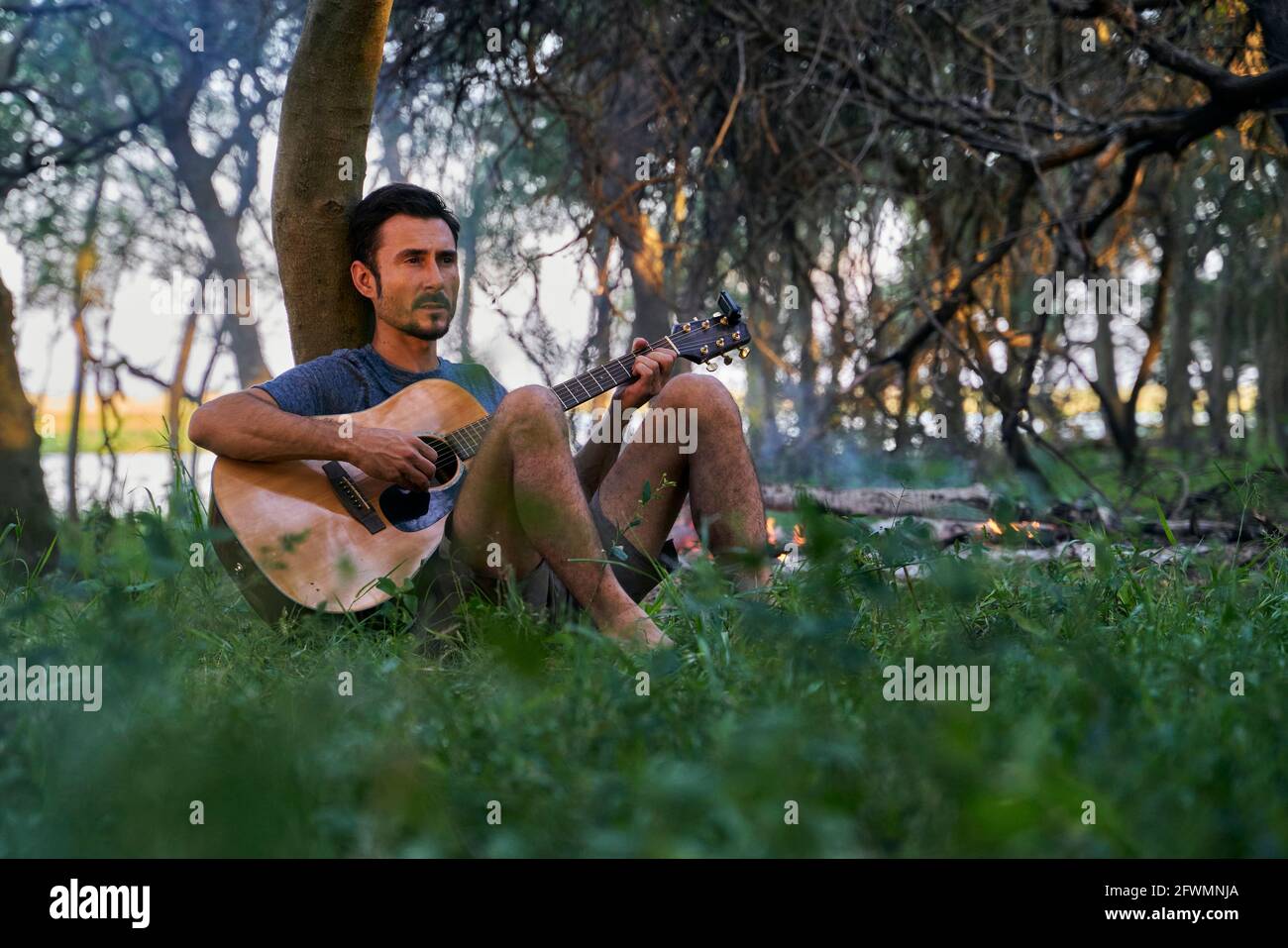 young man playing guitar sitting on a tree Stock Photo