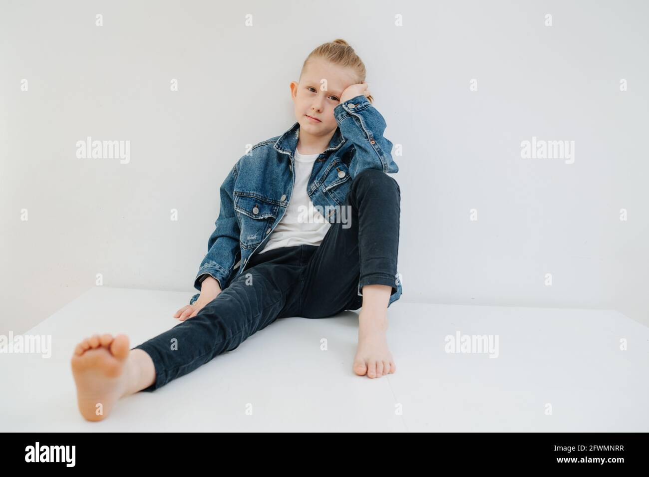 Portrait of a nine year old boy in a jeans suit. Sitting on a table. Over white. Stock Photo