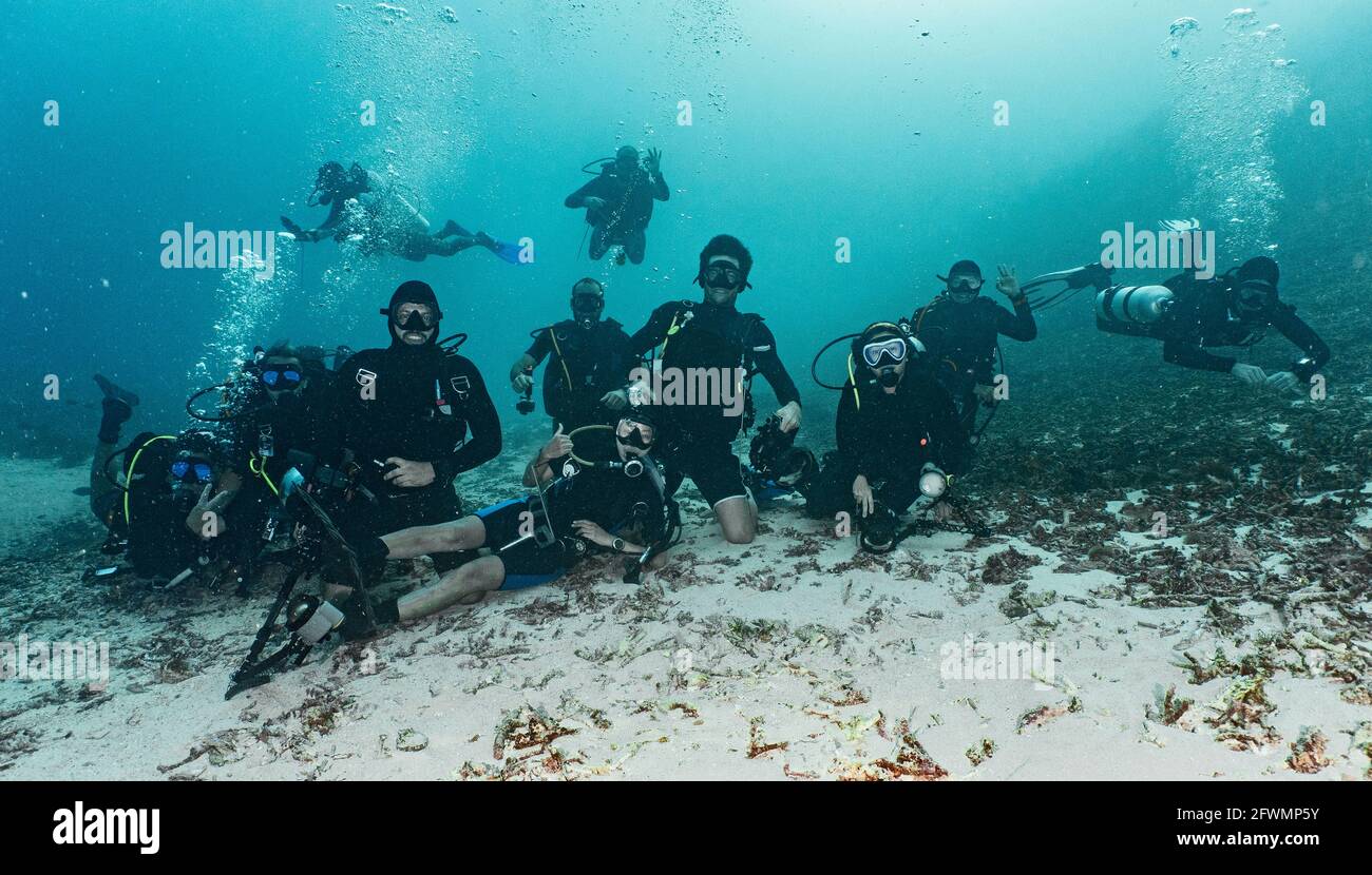 group of friends posing for camera on the ocean floor in Raja Ampat Stock Photo