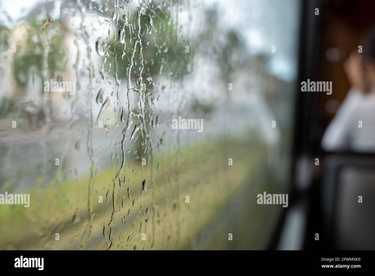 Close-up and macro view of raining water drop on outside windows of the tram or train and defocused background of indoor passenger train. Stock Photo