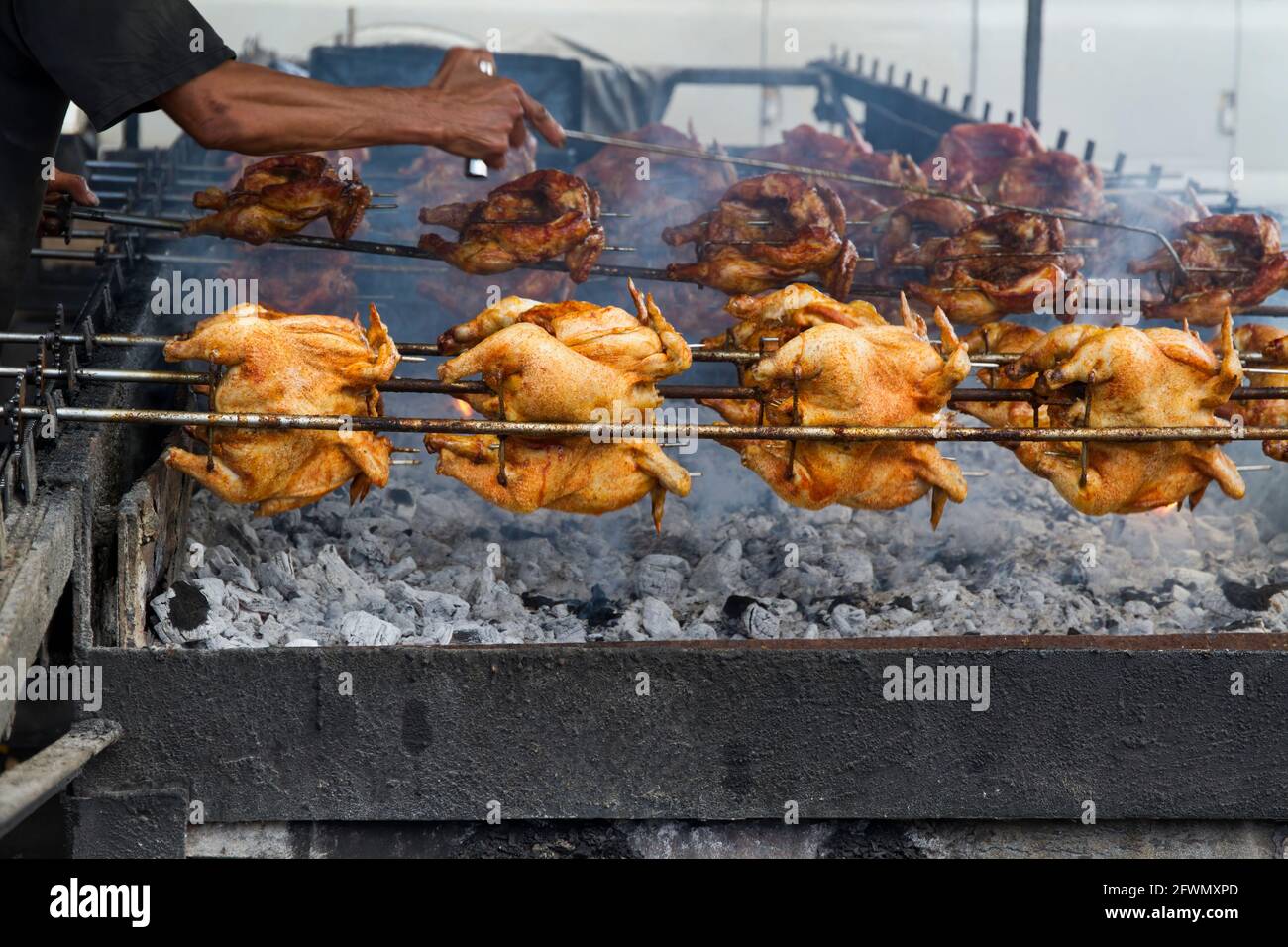 Street food vendor roasts whole chickens over charcoal pit on island of Oahu. Stock Photo