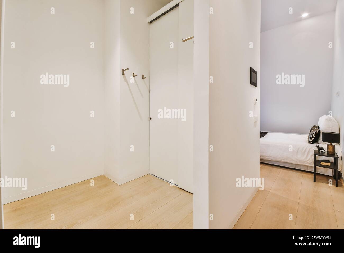 Interior of flat design with wooden floor and white walls in hallway and bedroom with simple bed
