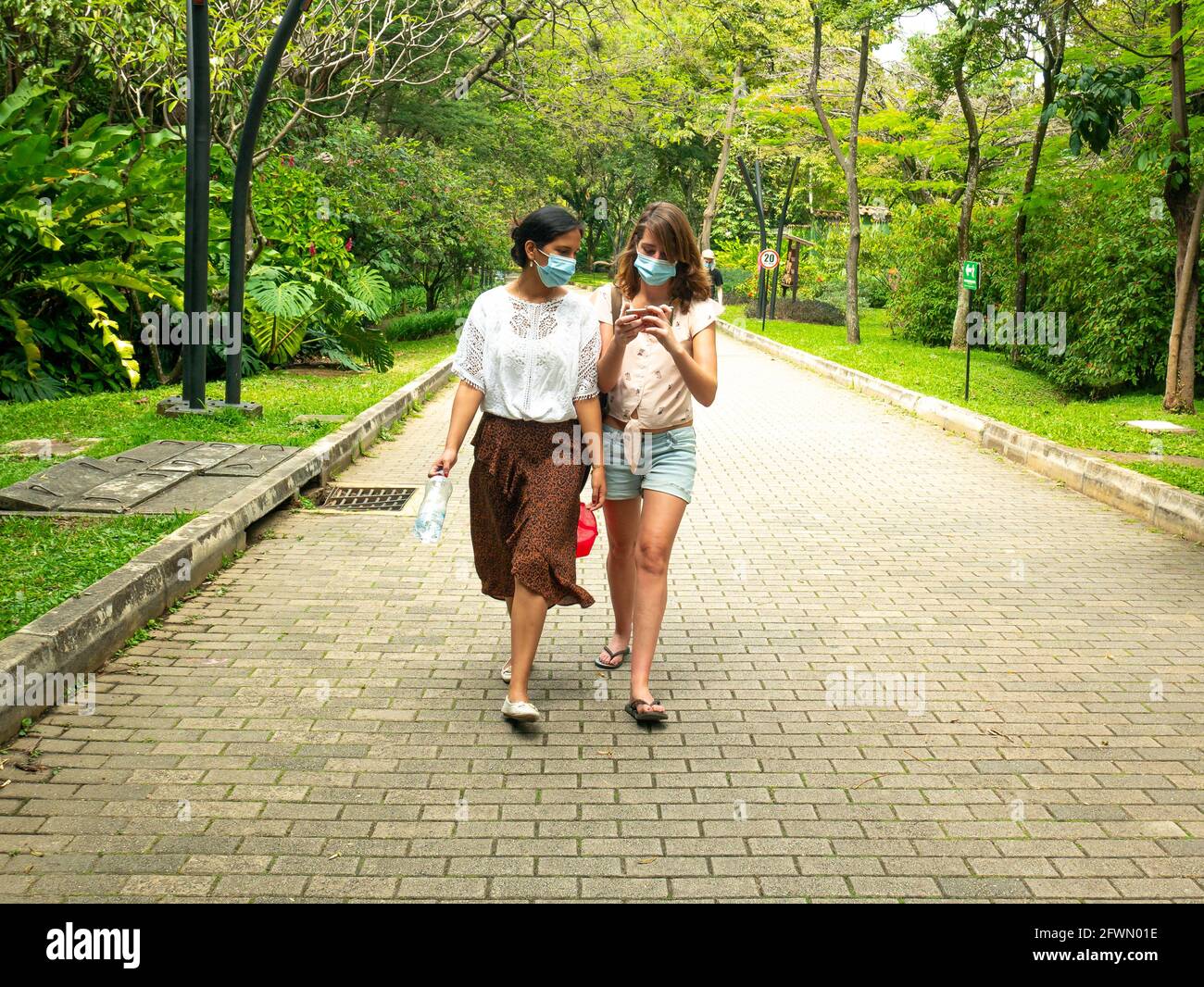 Medellin, Antioquia, Colombia - January 6 2021: Latin and Caucasian Women Wearing a Face Mask are Walking in a Park with a lot of Trees Stock Photo