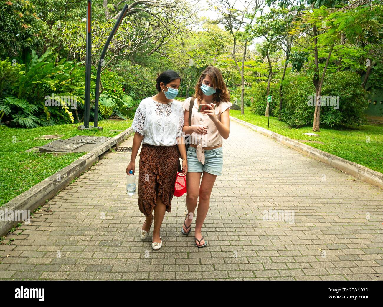 Medellin, Antioquia, Colombia - January 6 2021: Latin and Caucasian Women Wearing a Face Mask are Walking in a Park with a lot of Trees Stock Photo