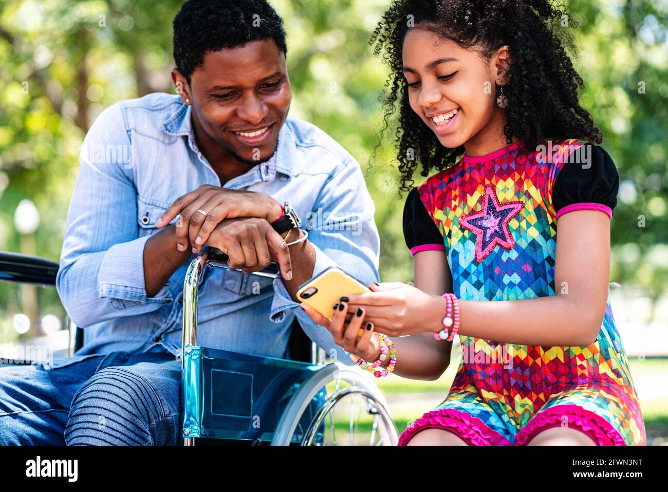 Man in a wheelchair using smartphone with her daughter Stock Photo - Alamy