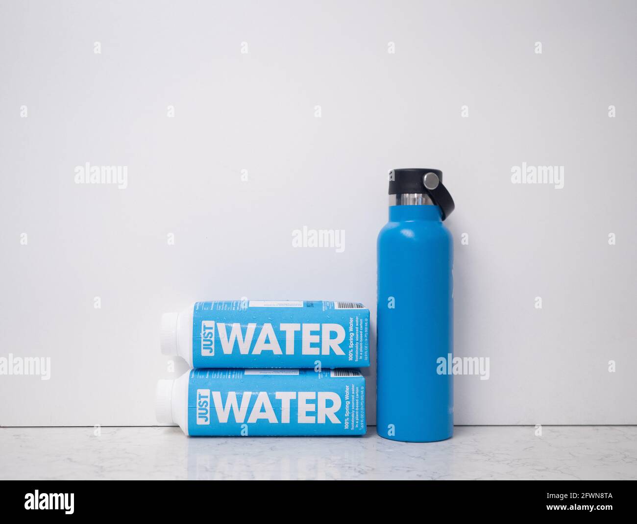 Two cardboard containers with water and a blue metal reusable container against a white background on a marble countertop. Stock Photo