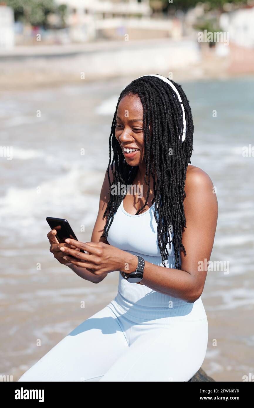 Joyful young woman sitting on beach and video calling her coach or friend Stock Photo
