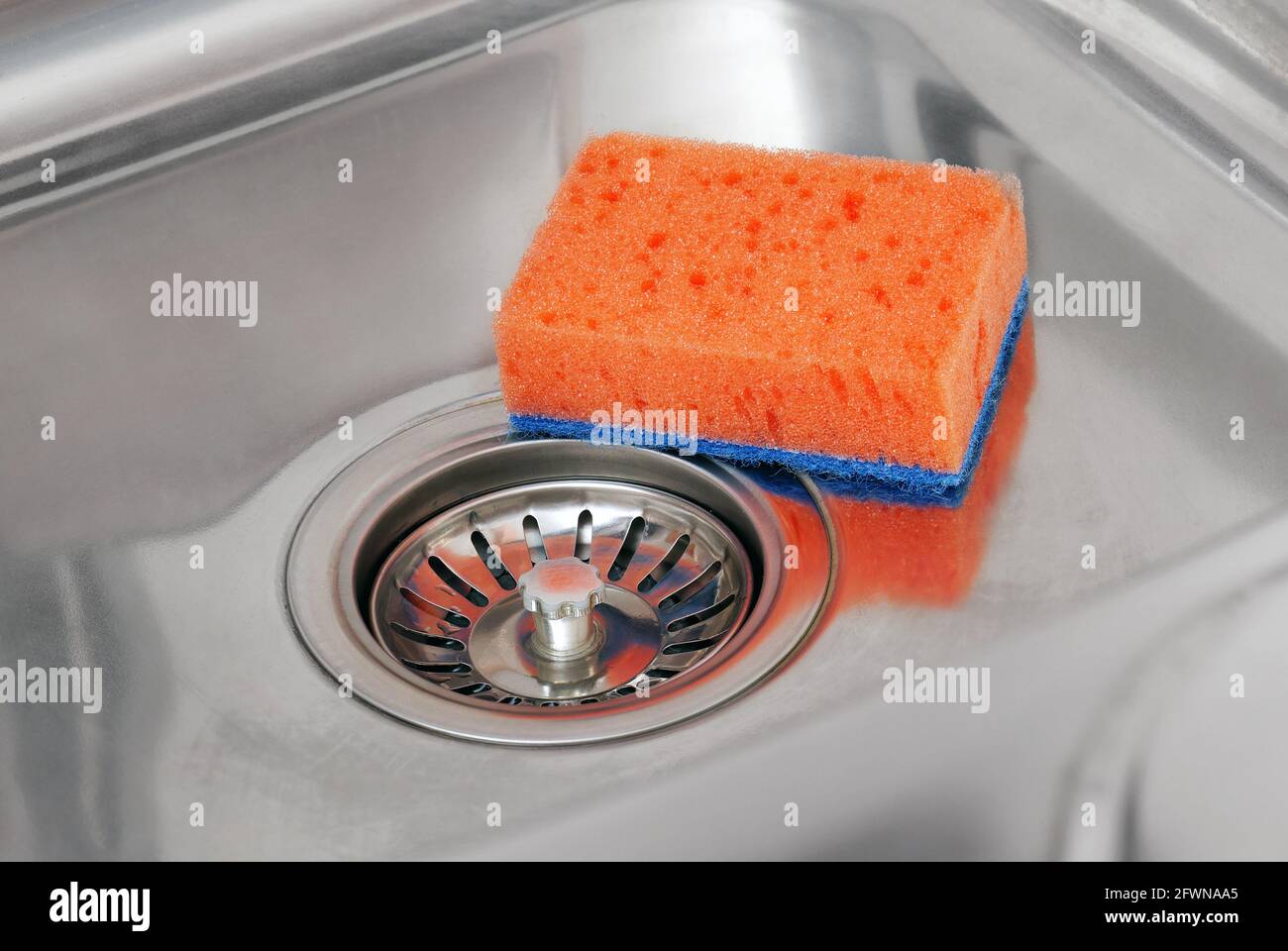 Closeup of orange sponge and strainer stopper in stainless steel sink