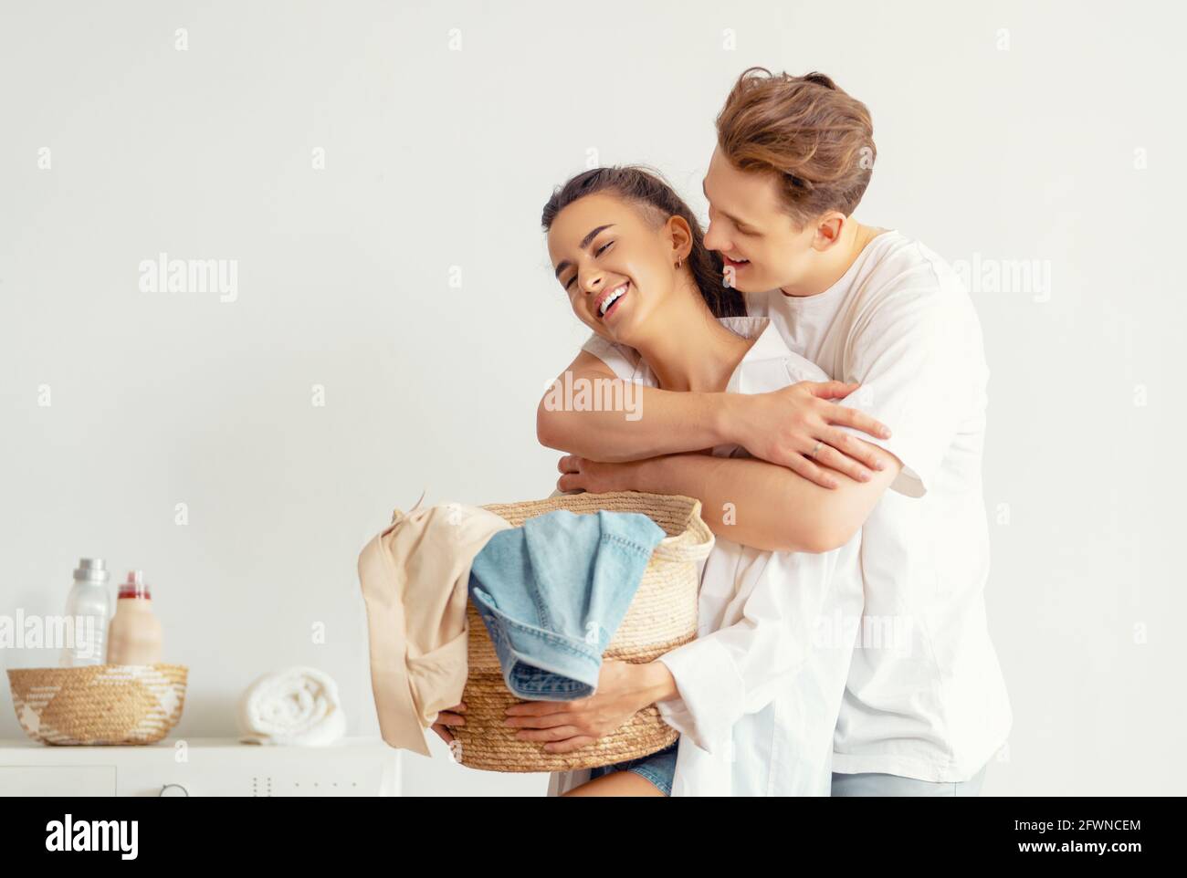 Beautiful young loving couple is smiling while doing laundry at home ...
