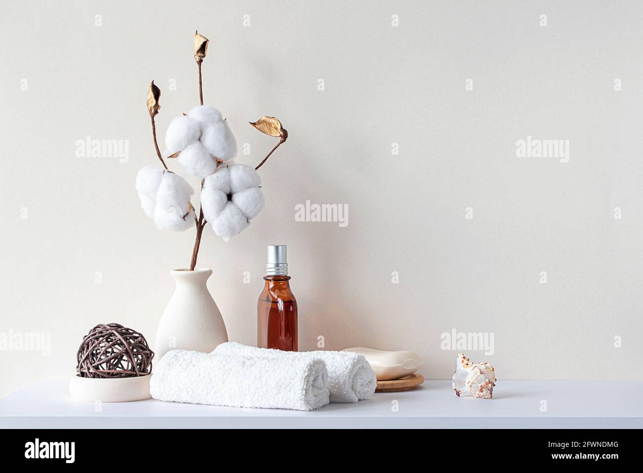 Bathroom interior in beige pastel tone. White shelf in bathroom with towels, soap, perfume bottle, cotton plant. Mockup with space for text. Minimal c Stock Photo