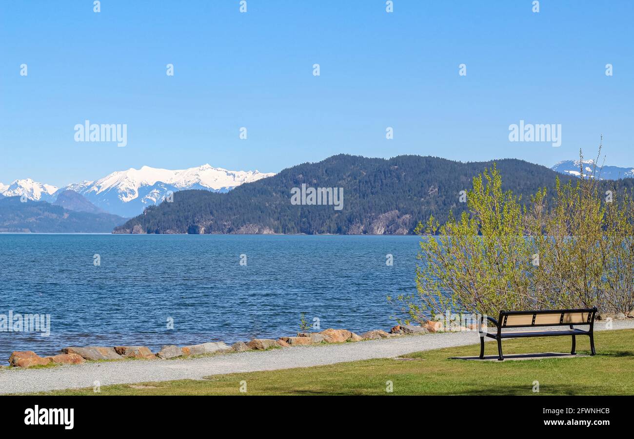 Beautiful landscape of the Harrison Lake and mountains on the background. Empty bench on the beach of the lake. Travel photo, street view, selective f Stock Photo