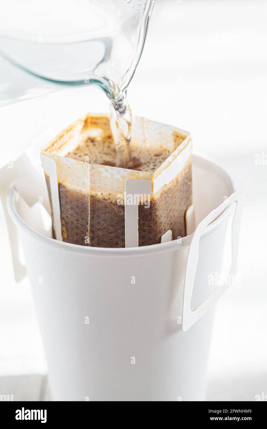Making coffee with drip coffee bag in a white paper cup. Drip brewing