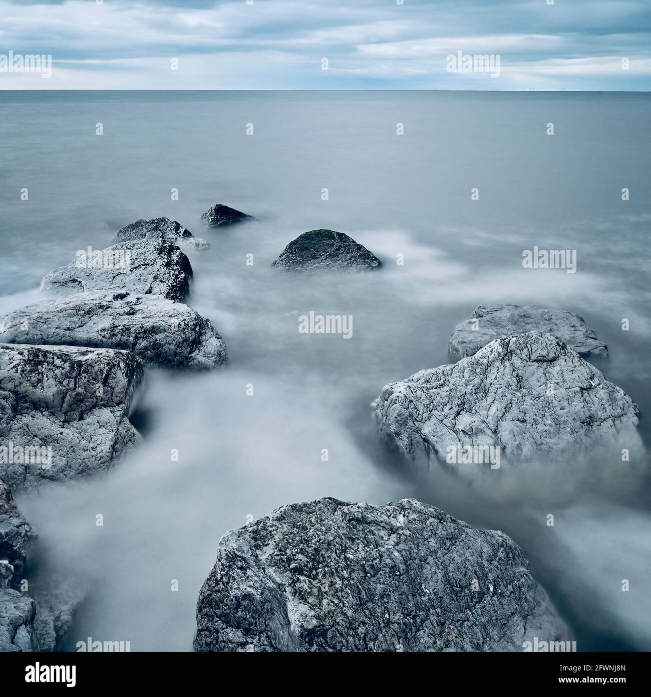 Long exposure of grey rocks in sea with water swirling round Stock ...