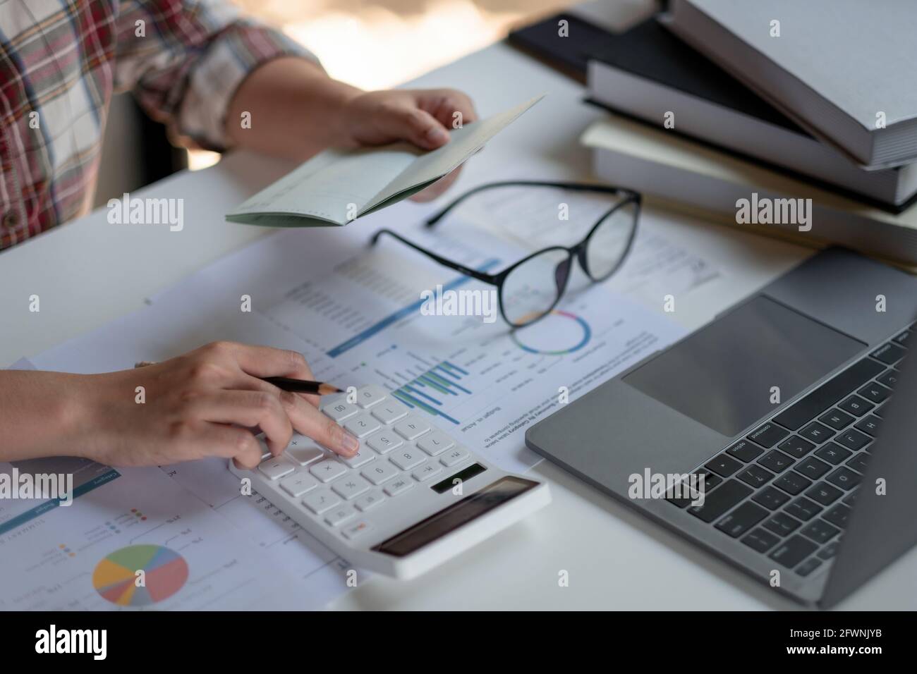 woman checking amount in bank account passbook with bank statement. Accountant using calculator for financial Stock Photo