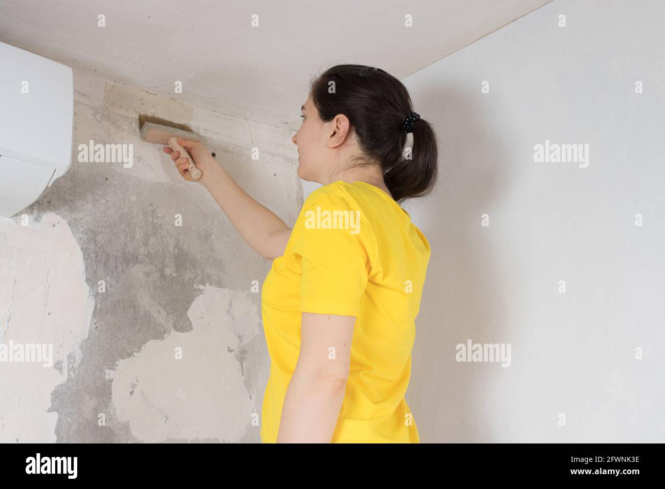 Woman repairman smears the wall with glue. Sticking wallpaper in the
