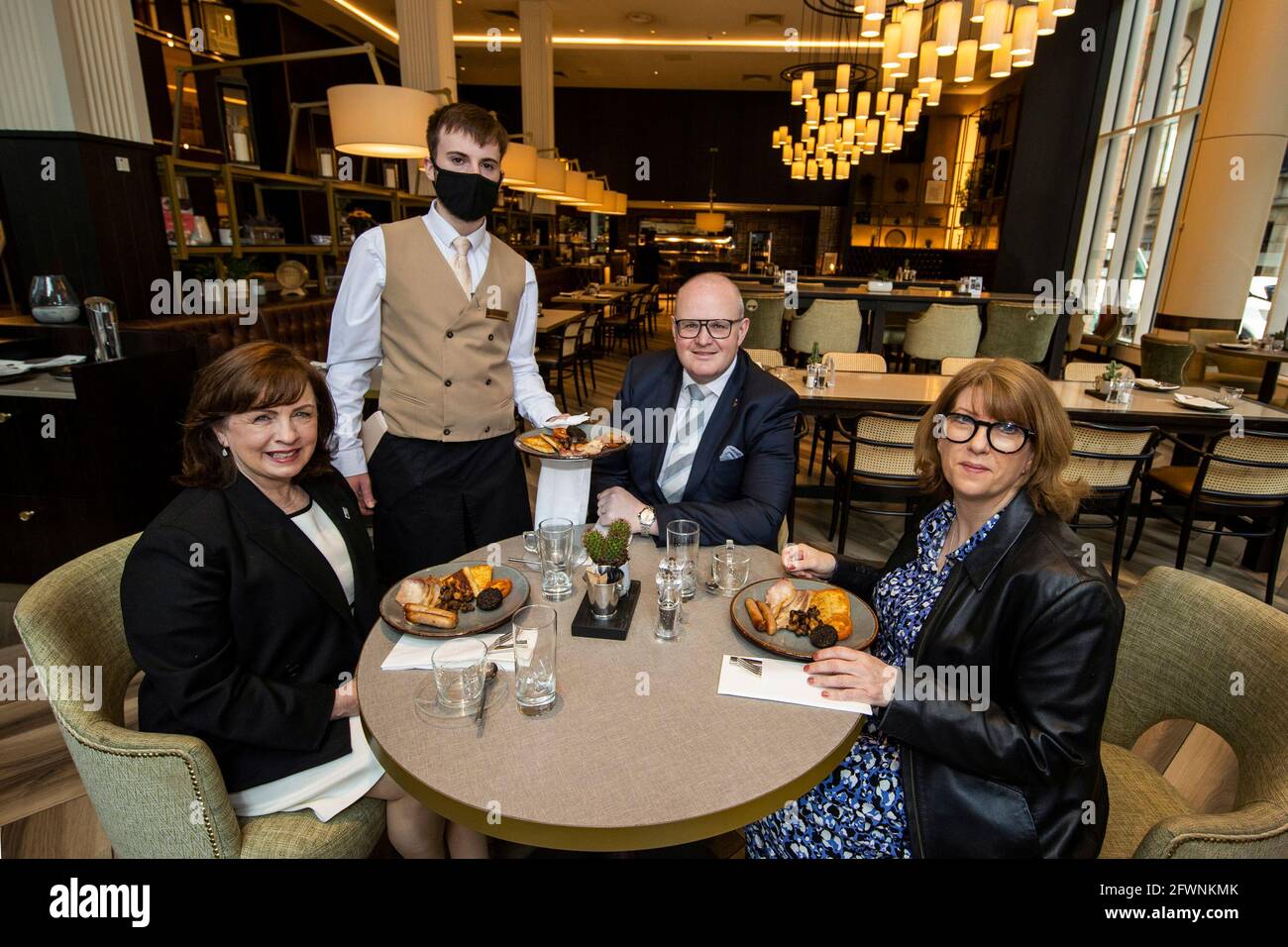 Northern Ireland Economy Minister Diane Dodds (left) welcomes the reopening of indoor hospitality at the Grand Central Hotel in Belfast with Janice Gault (right) of the Northern Ireland Hotels Federation (NIHF) and General Manager Stephen Meldrum (second from right) as they are being served the hotel's house breakfast by Conor Sullivan. Stock Photo
