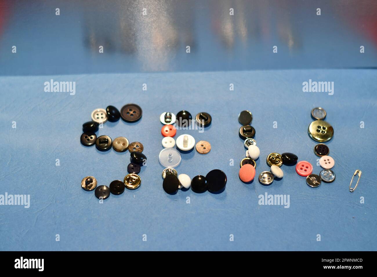 sew letters in an array of clothes buttons on a blue back ground with a safety pin Stock Photo