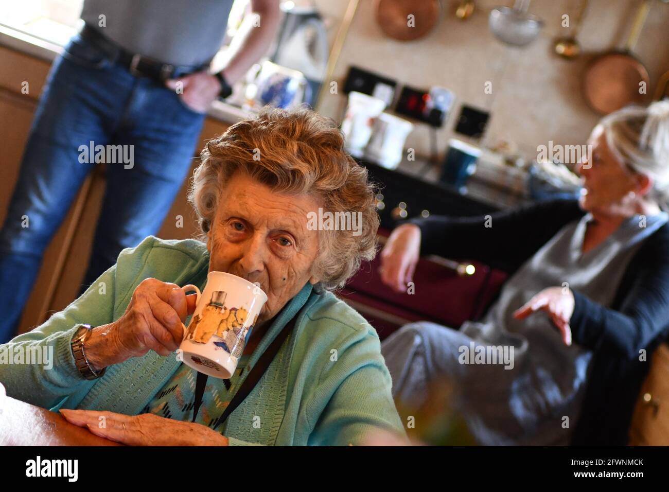 Senior woman enjoying cup of tea with family chatting in the background Stock Photo
