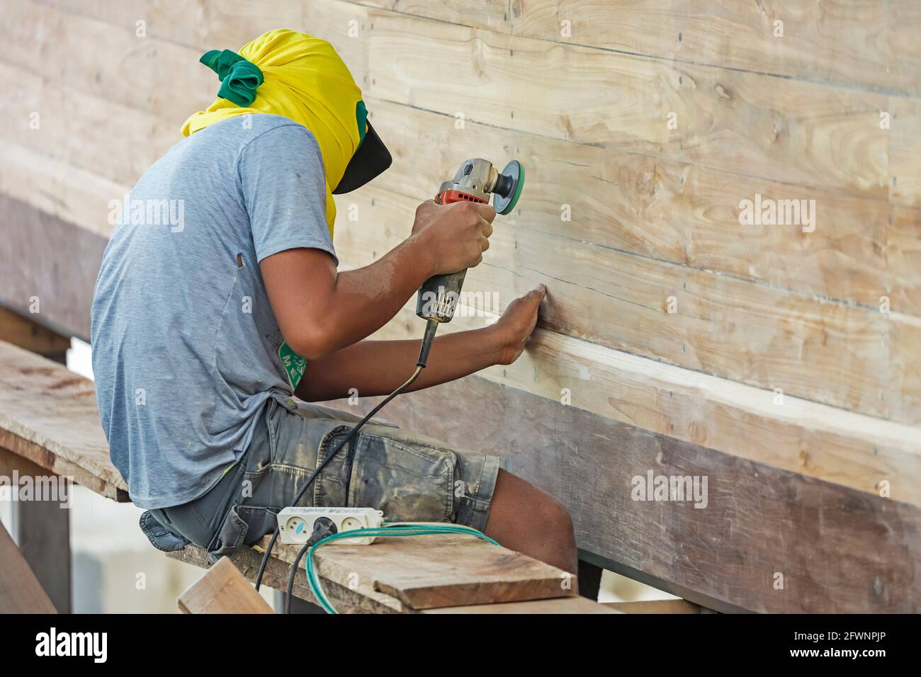 Boatbuilder with angle grinder tool sanding a classic phinisi schooner in this southern resort town's harbour; Tanjung Bira, South Sulawesi, Indonesia Stock Photo