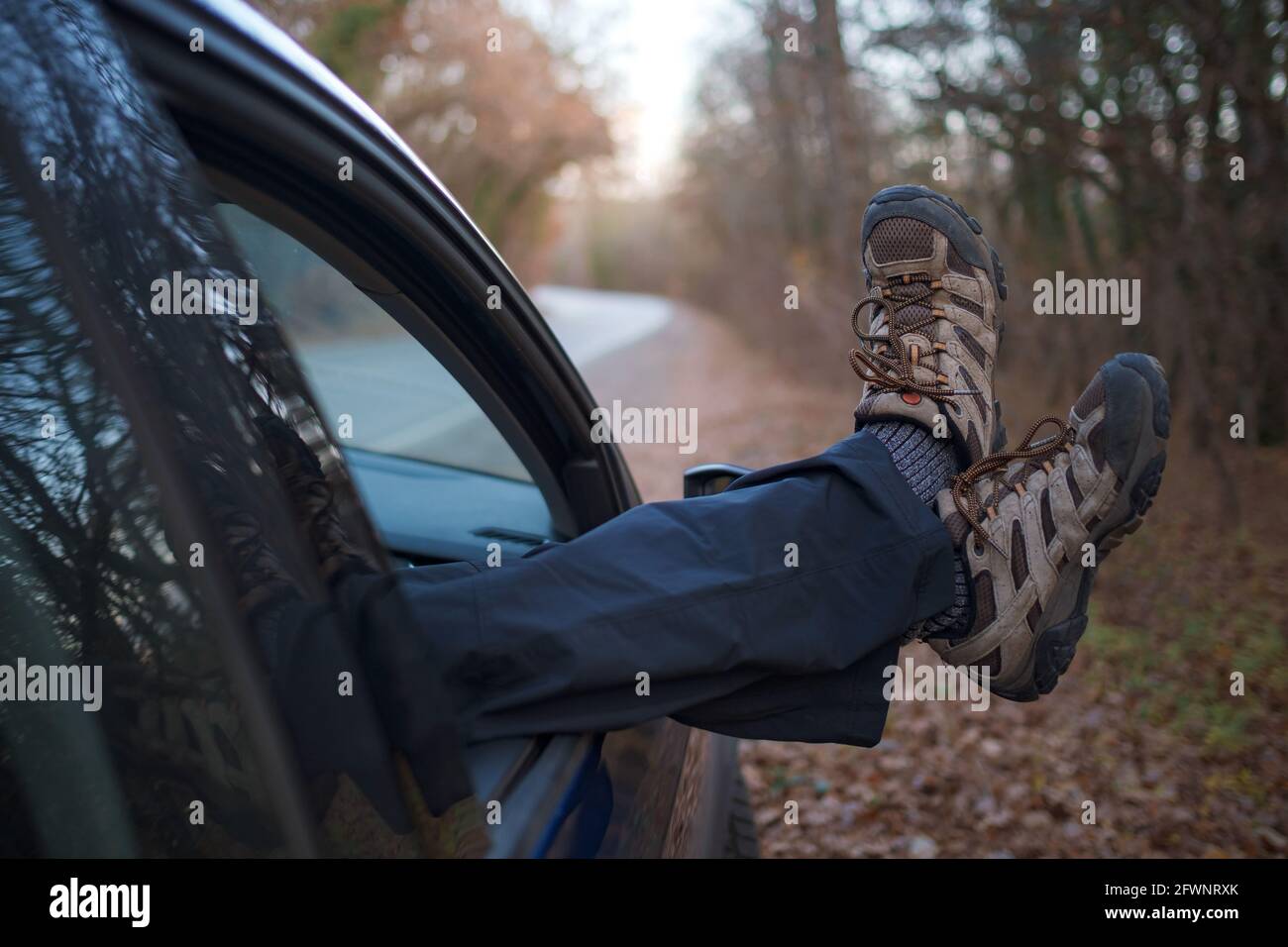 male feet in trekking boots sticking out the car window. Autumn car