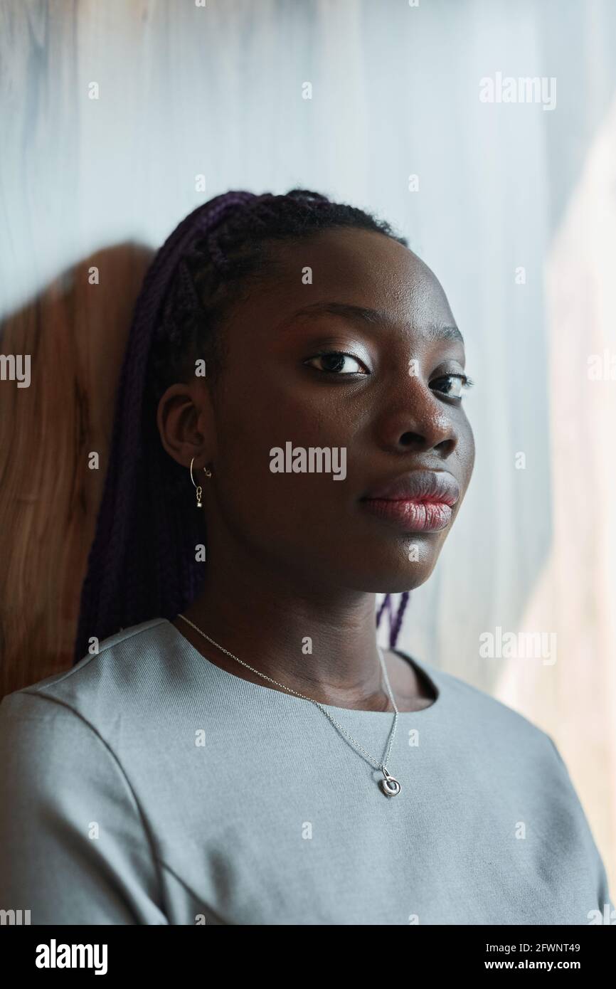 Graphic head and shoulders portrait of confident African-American woman looking at camera while standing by window in sunlight Stock Photo