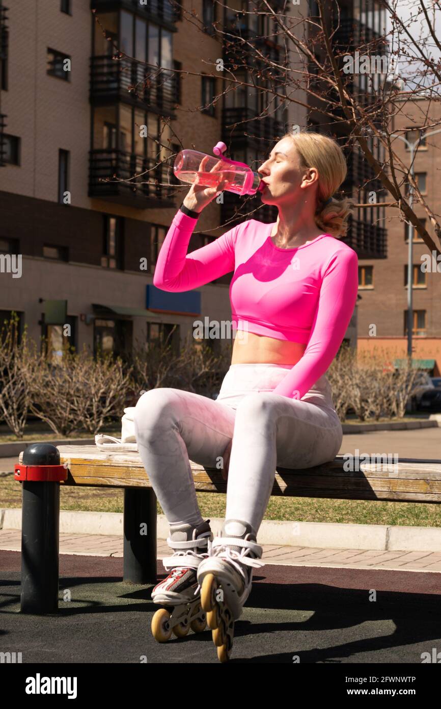 Young tired woman in trendy sportswear and roller skates drinks clean water  from a sports bottle. Active healthy lifestyle fitness workout skates dail  Stock Photo - Alamy