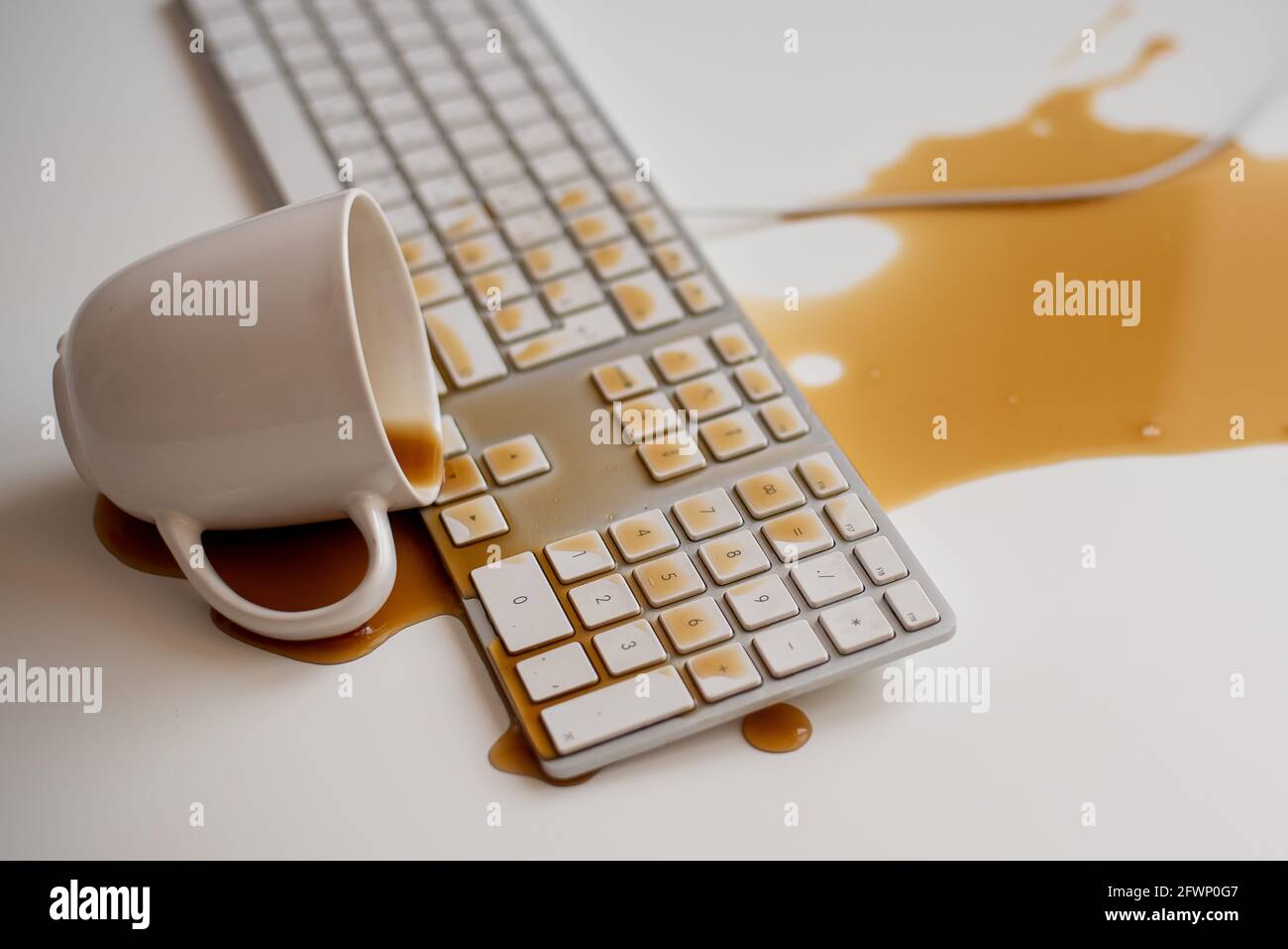 Spilled black coffee on a computer keyboard at a white table Stock