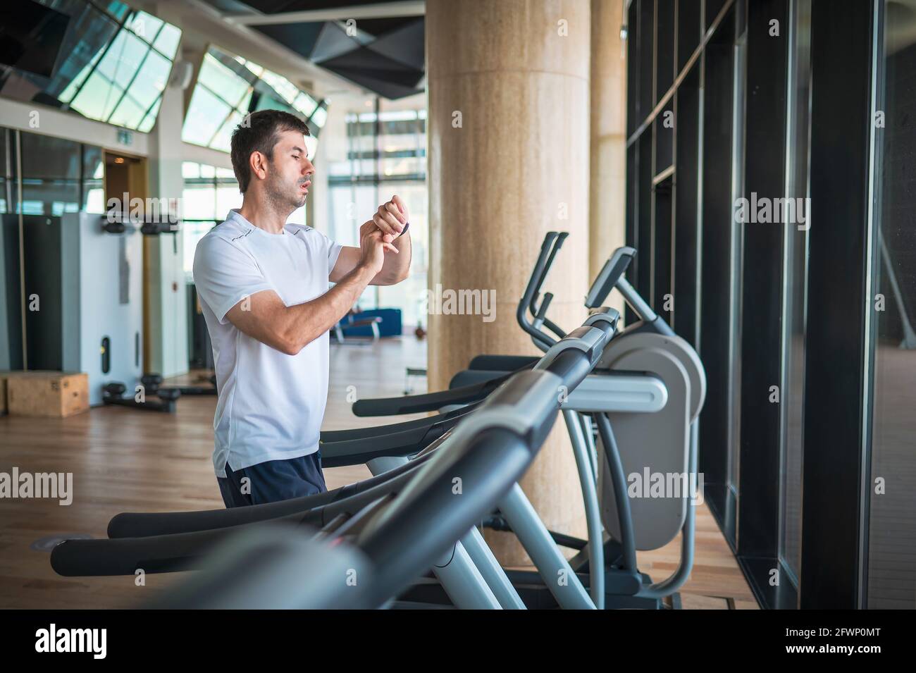 Man using smart watch fitness tracker device while jogging on a treadmill during a cardio running warmup exercise in the gym for staying fit and in sh Stock Photo