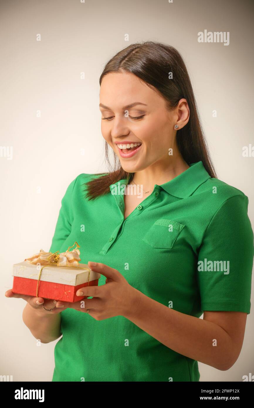Young woman portrait hold gift in christmas color style . Smiling happy girl onn a light grey background Stock Photo