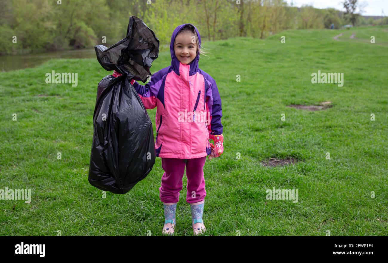 A little girl with a garbage bag on a trip to nature to clean the environment. Stock Photo
