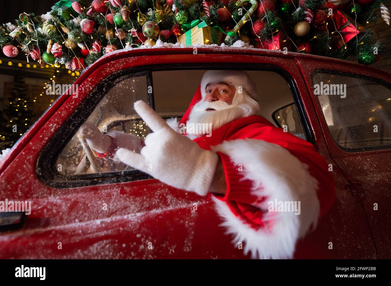 Portrait of santa claus driving a car loaded with a Christmas tree and
