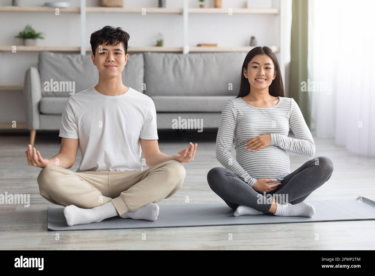 Positive pregnant asian couple doing yoga together Stock Photo