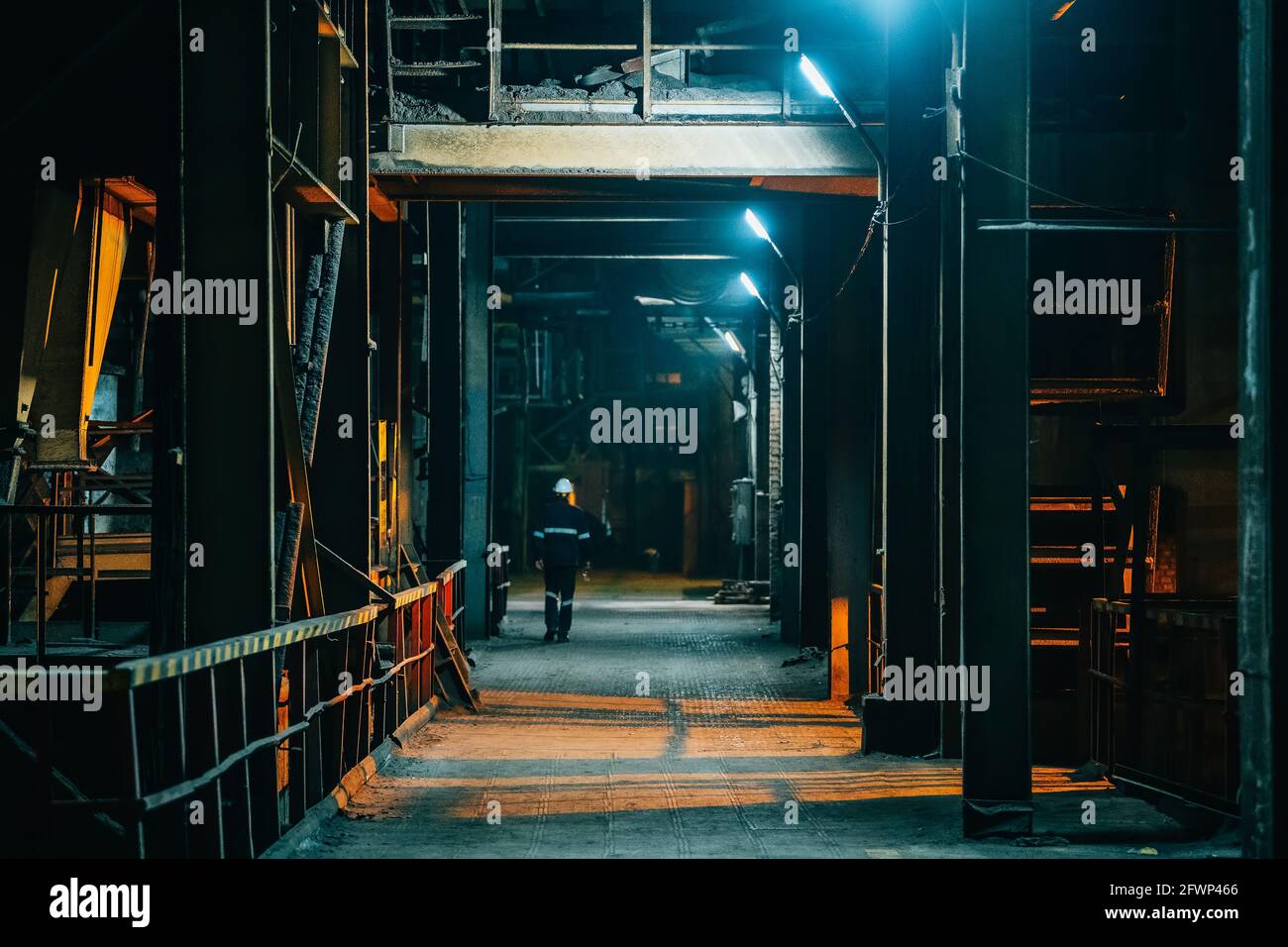 Dark creepy industrial corridor with lamp illumination and silhouette of worker man in distance. Stock Photo