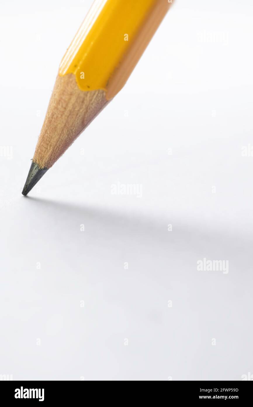 Pencil stands on white paper. The sharp point has just been sharpened. Focus on the black graphite tip. Vertical background image Stock Photo