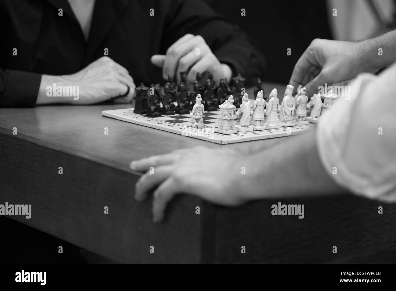 Grayscale shot of two people hands playing chess on the table Stock Photo