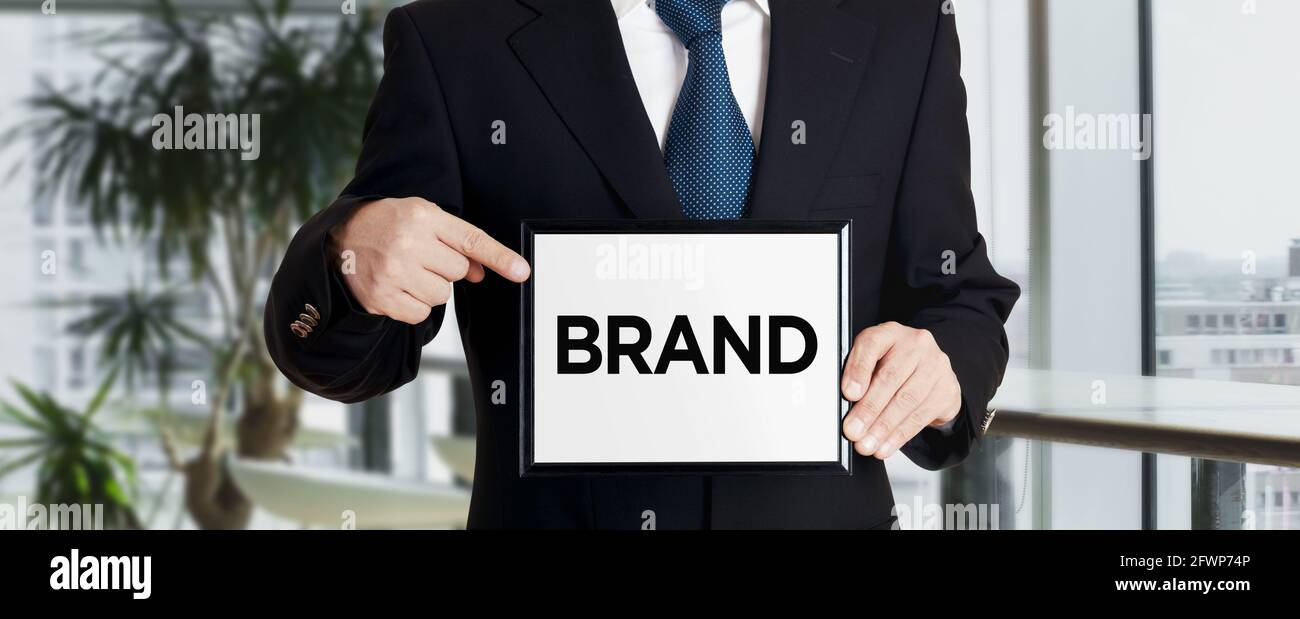 Businessman holds a signboard and points his finger to the word brand. Business marketing concept. Stock Photo
