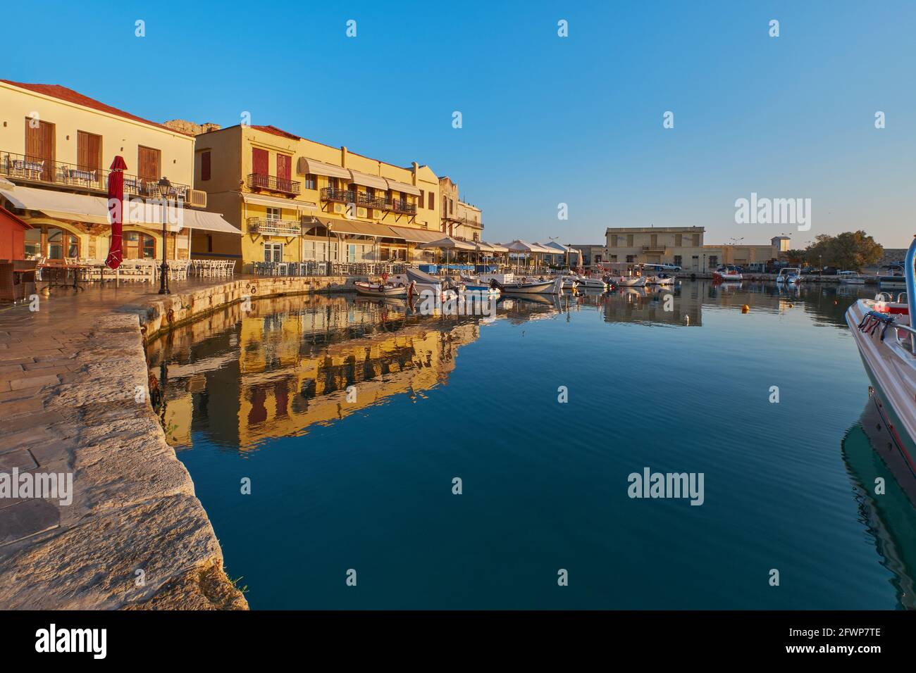 the quay of the historic port of Rethimno in the morning sun, boats in the port and empty restaurants Stock Photo