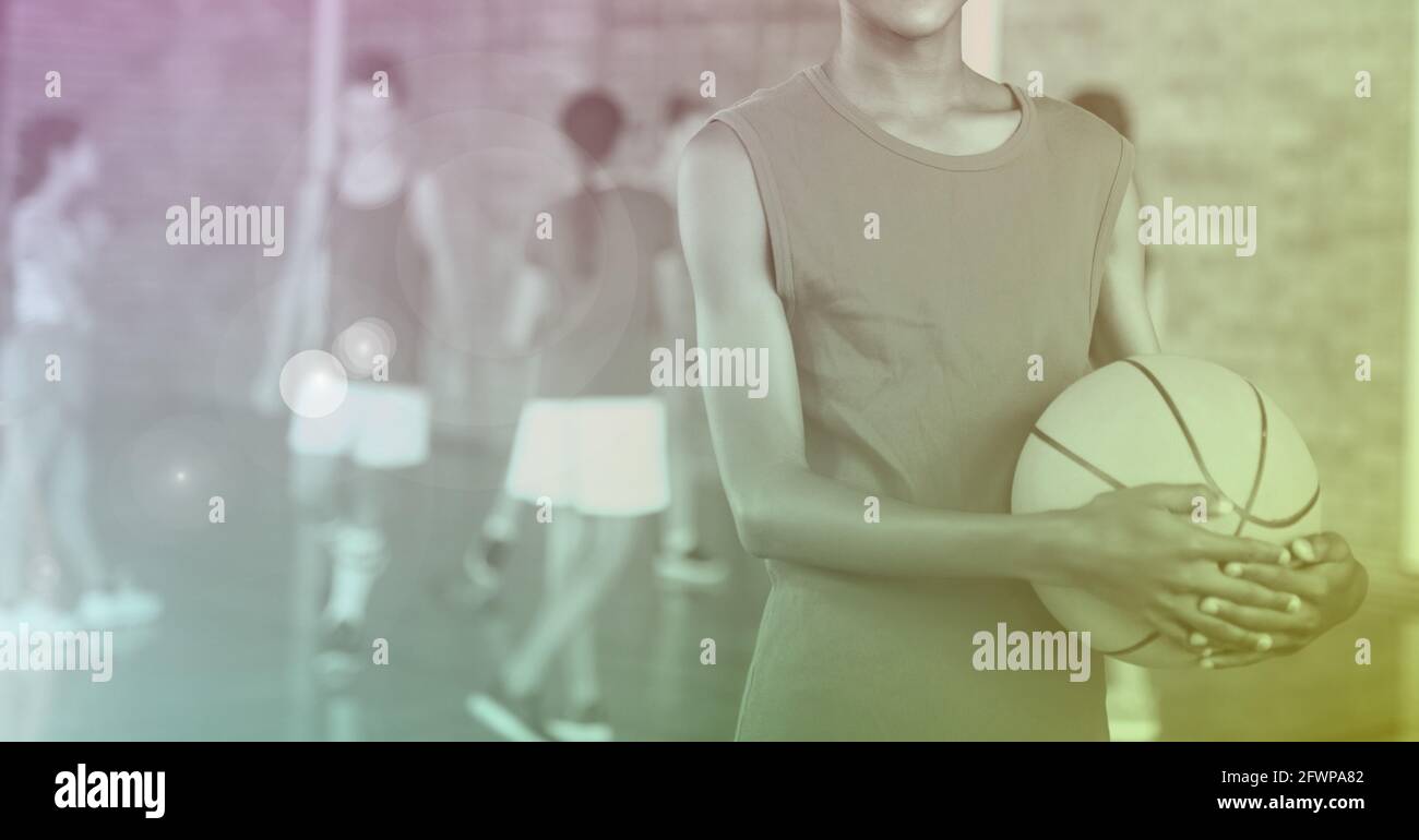 Composition of midsection of school basketball player holding ball with purple tint Stock Photo