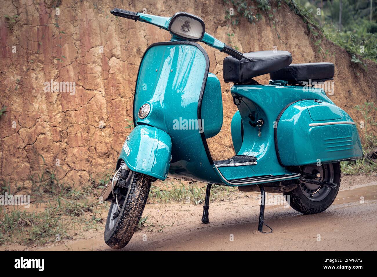 Vespa Scooter front view, parked in a muddy road on a rainy day. Sky blue vintage classic motorbike. Stock Photo