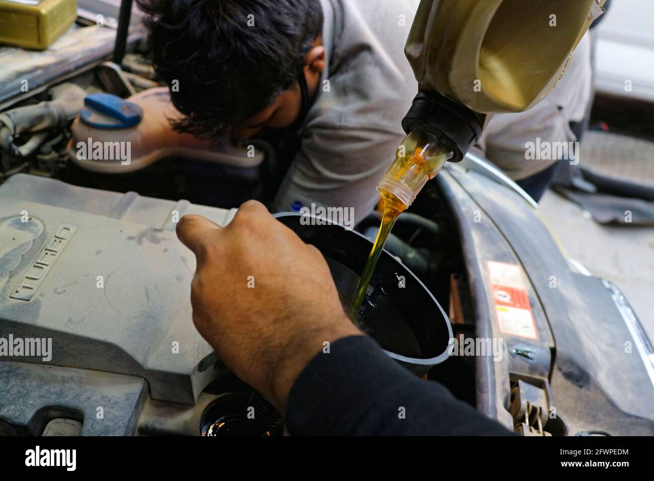 Kuwait City – Kuwait – April 15, 2021: Mechanic working on car while another pours engine oil Stock Photo