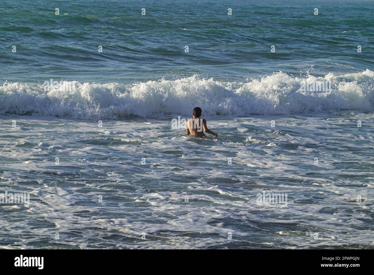 Rear view of a young man swimming on the sea with waves splashing Stock ...