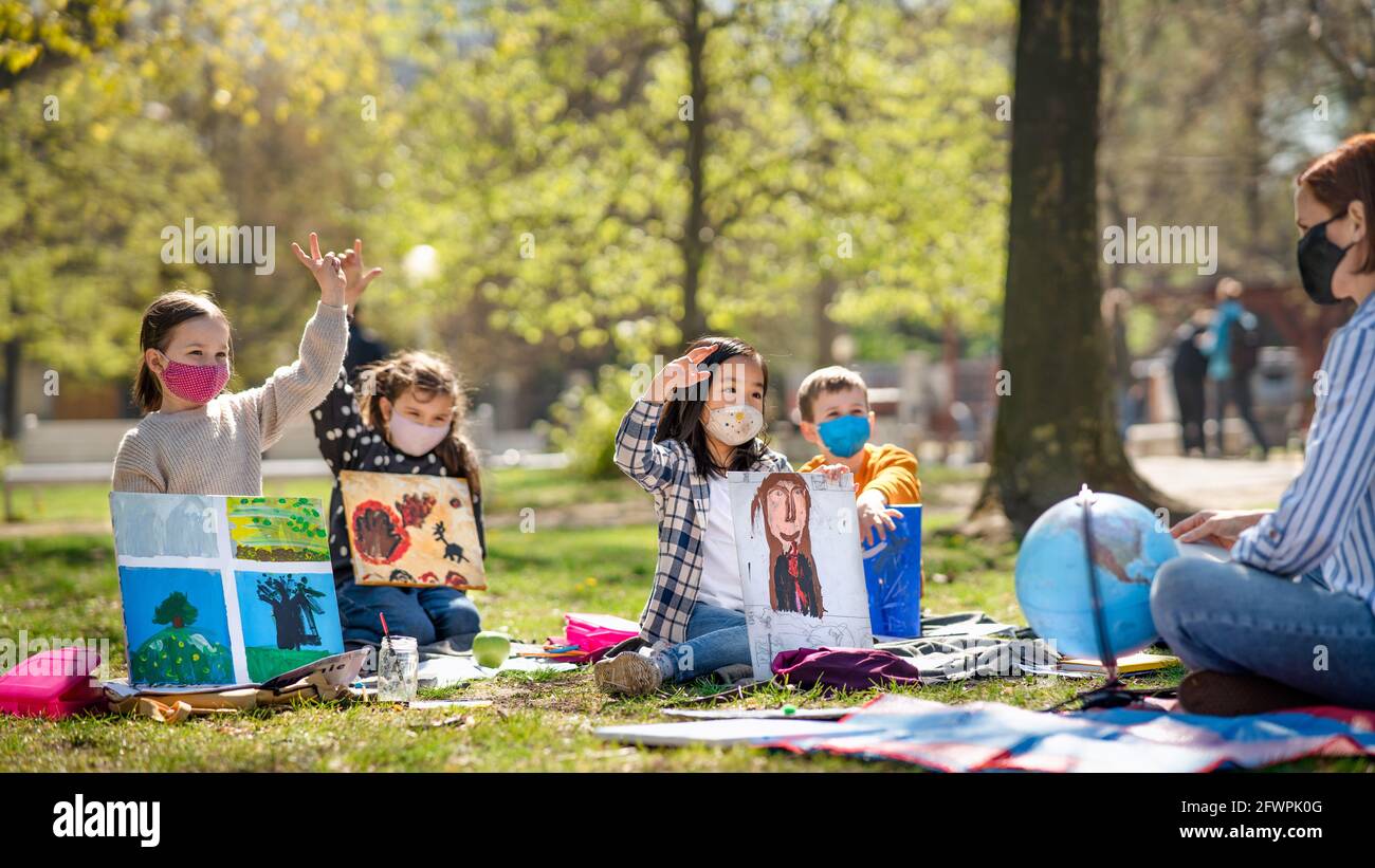 Small children with teacher outdoors in city park, learning group education and coronavirus concept. Stock Photo