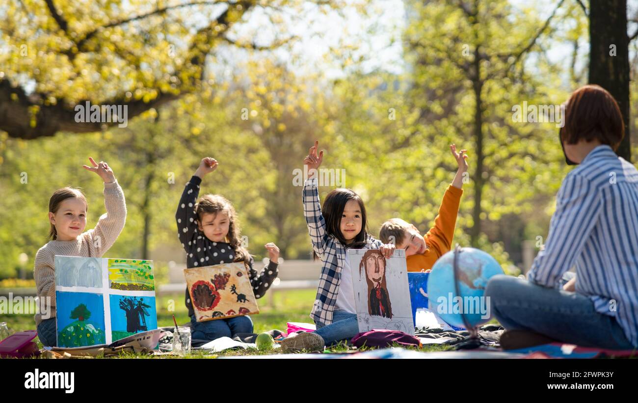 Small children with teacher outdoors in city park, learning group education and art concept. Stock Photo