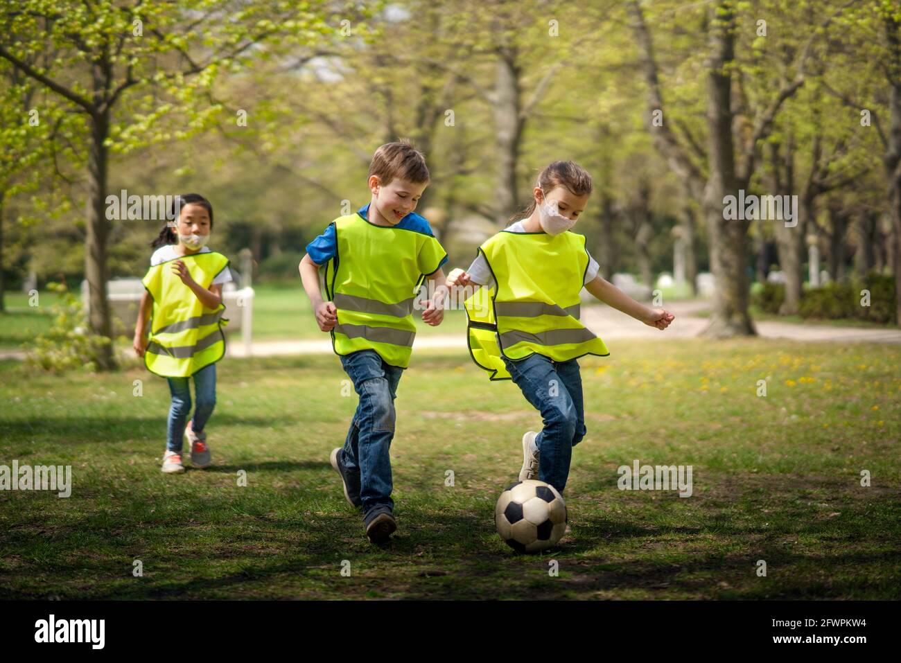 Small children playing football outdoors in city park, learning group education concept. Stock Photo