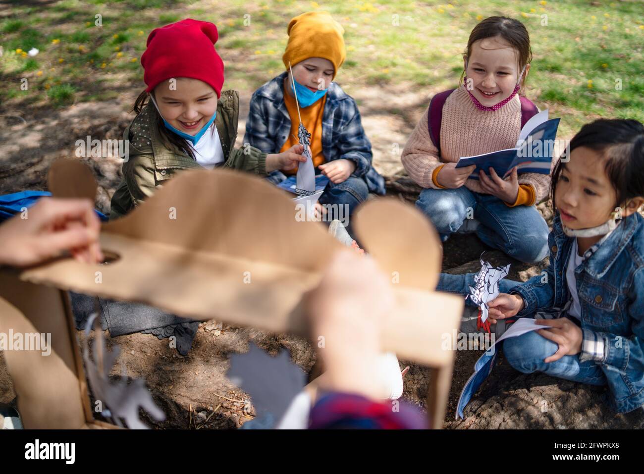 Teacher with small children sitting outdoors in city park, learning group education and coronavirus concept. Stock Photo