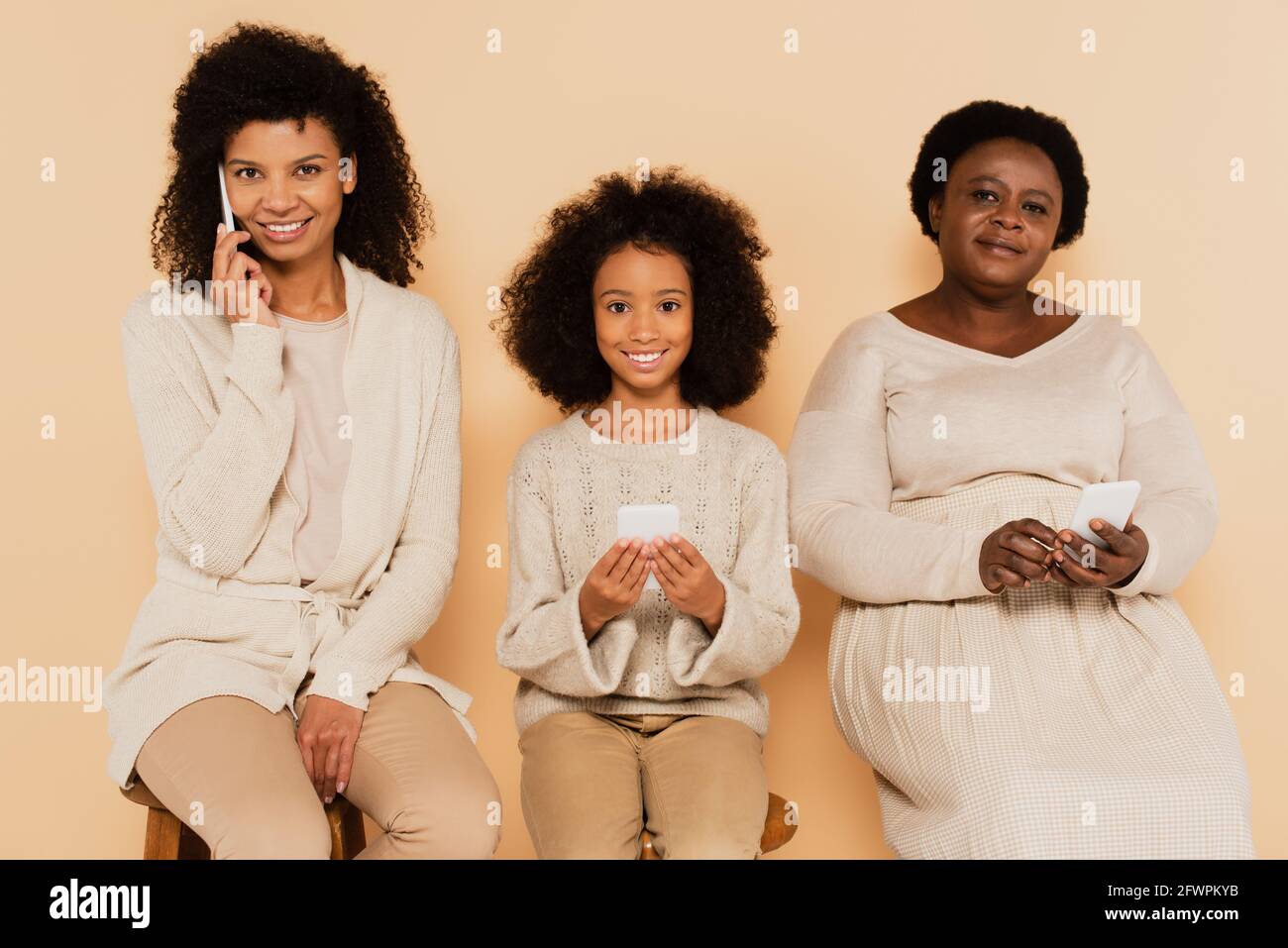 african american mother speaking on cellphone near daughter and grandmother with smartphones in hands on beige background Stock Photo