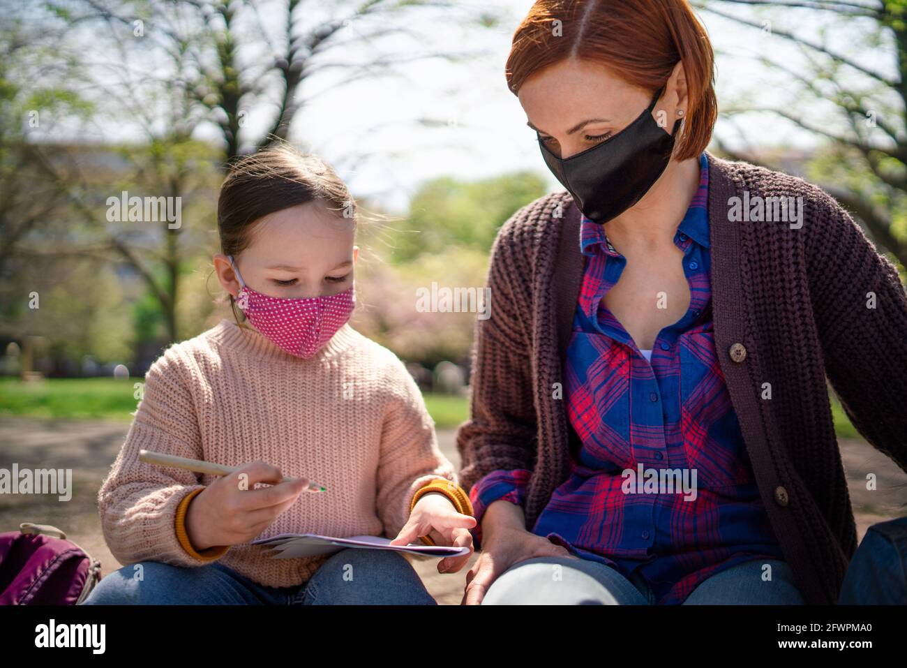 Teacher with small child sitting outdoors in city park, learning group education and coronavirus concept. Stock Photo