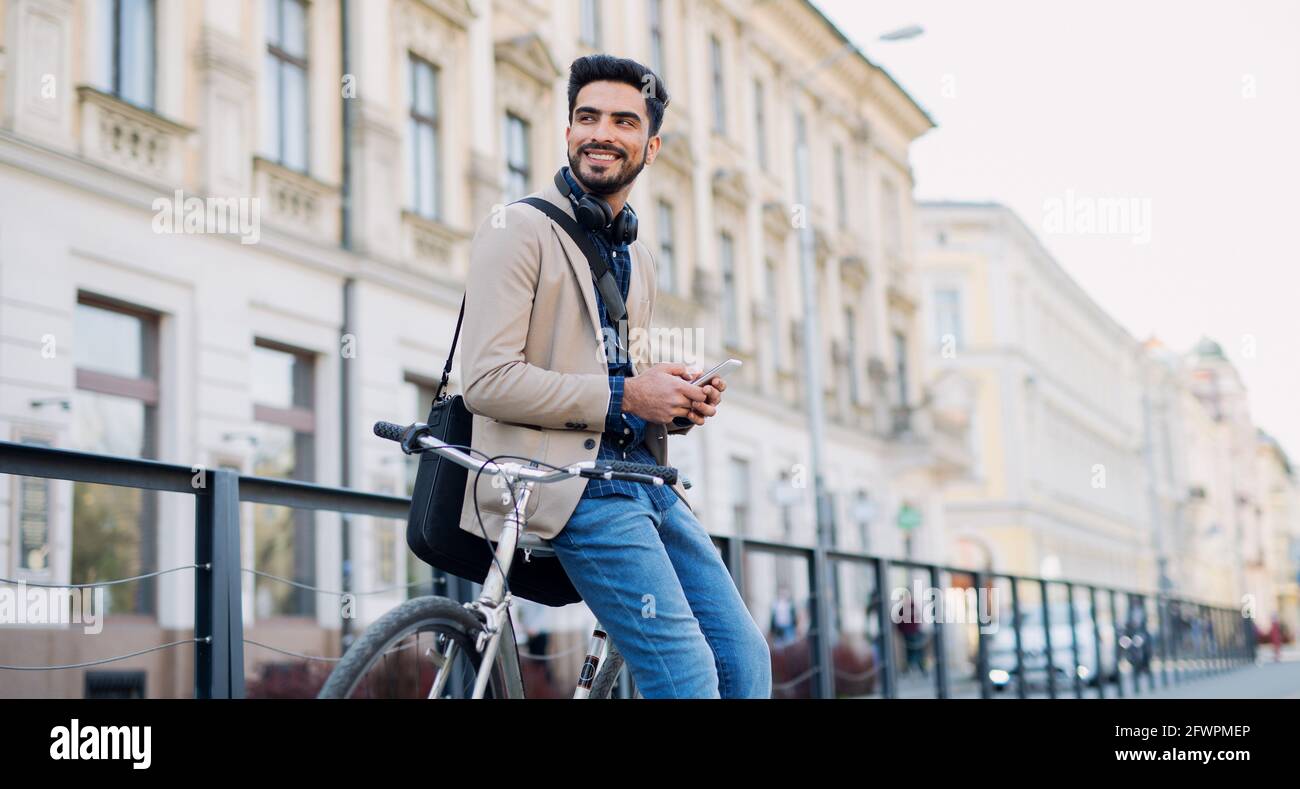 Young business man commuter with bicycle going to work outdoors in city, using smartphone. Stock Photo
