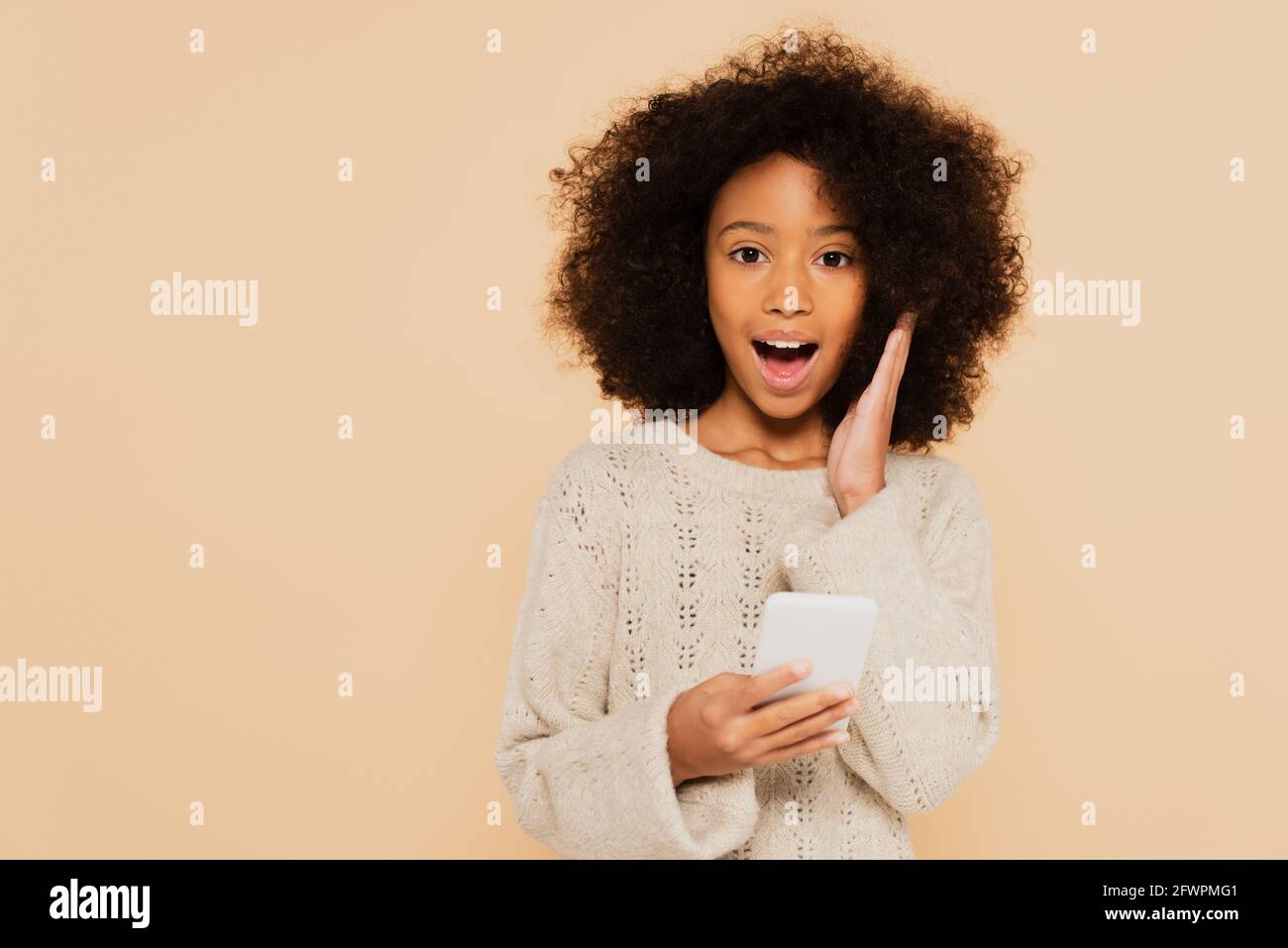 excited african american preteen girl with hand near face holding ...